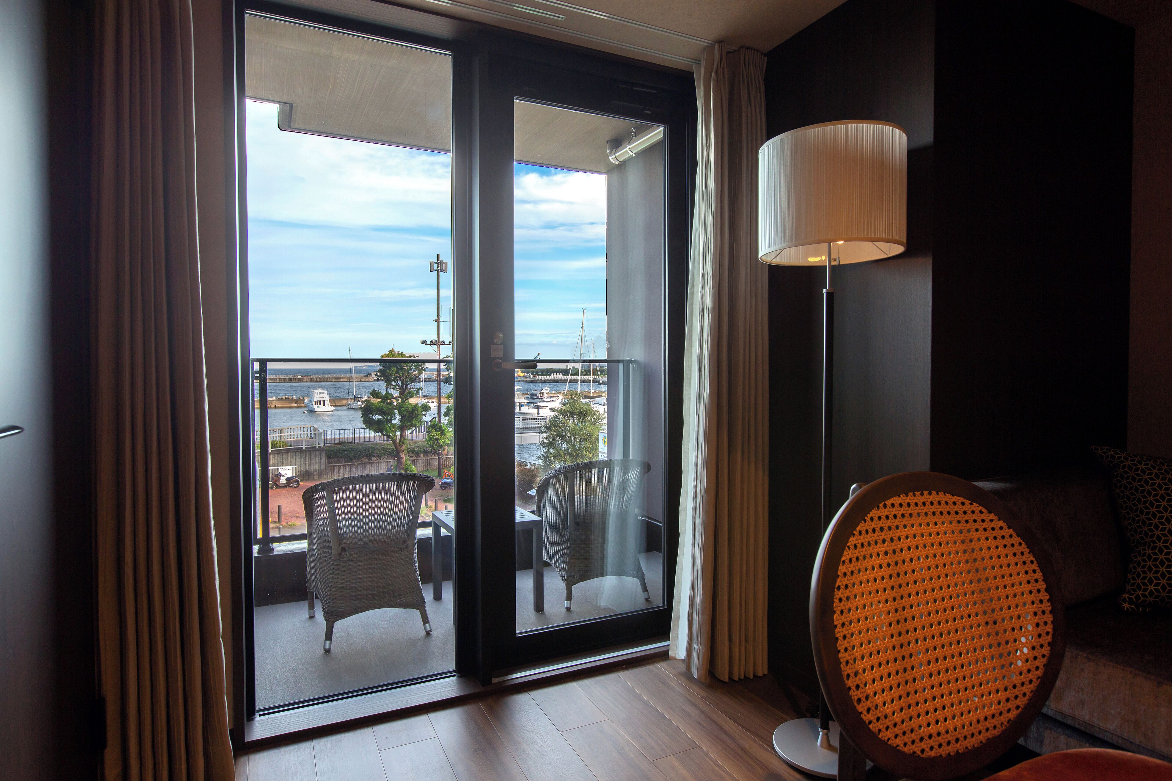 A room with a balcony, a wicker chair, a sofa, and a floor lamp.