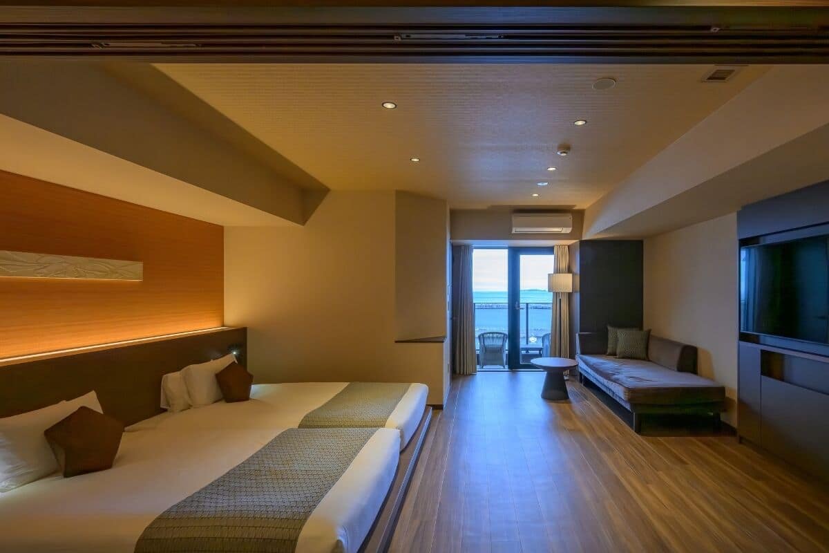 Habitación de hotel con una cama grande, un sofá, un televisor y un balcón con vistas.