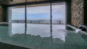 Una piscina interna con vista sul mare, pareti in pietra e soffitto in legno.
