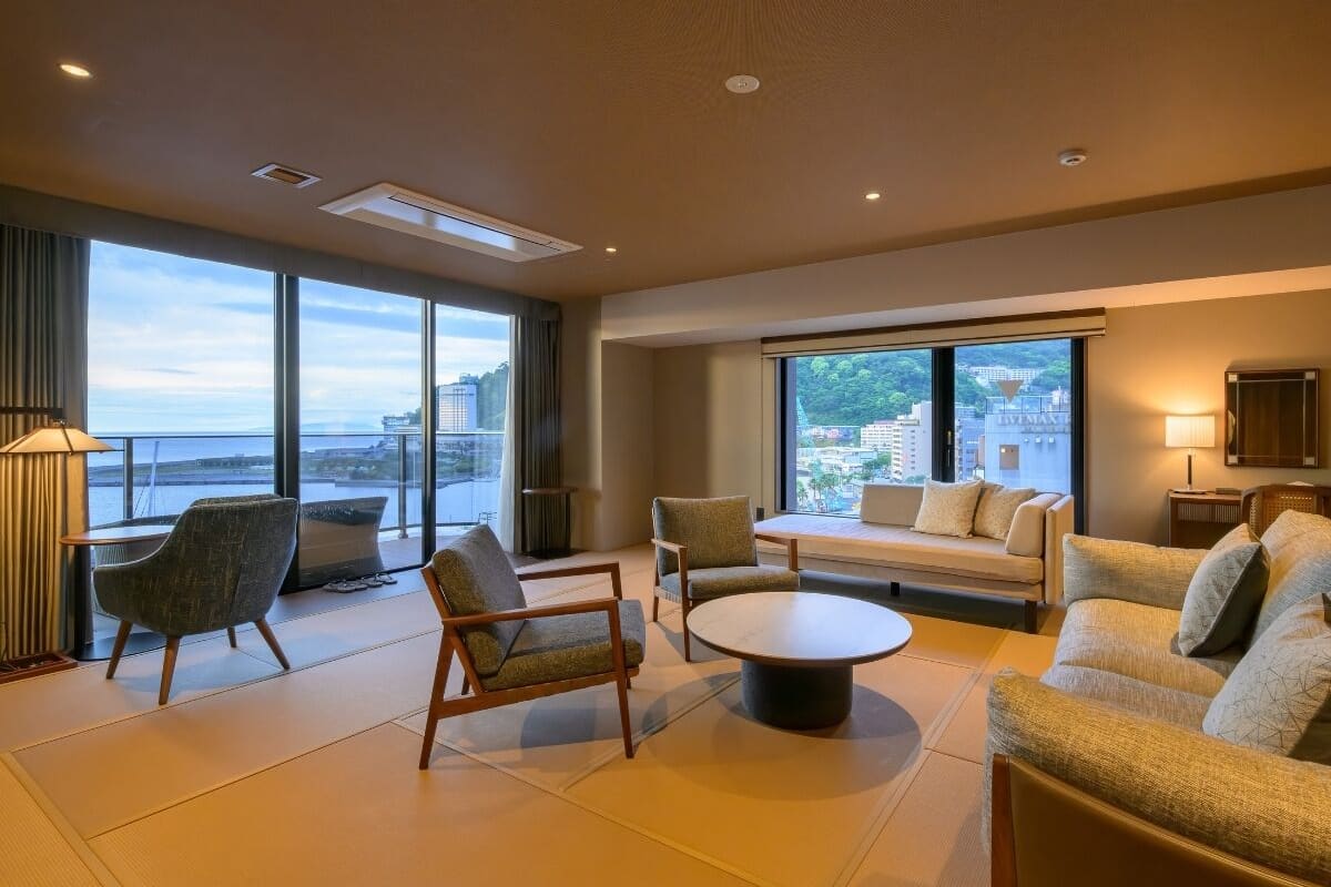 Amplia sala de estar con sofá, sillas, una mesita de centro y ventanas amplias con vistas a la ciudad.