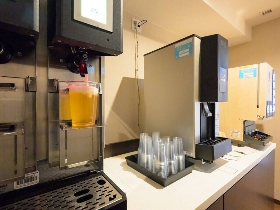 Una máquina de café sirviendo una bebida, una pila de vasos de plástico y un dispensador de bebidas.