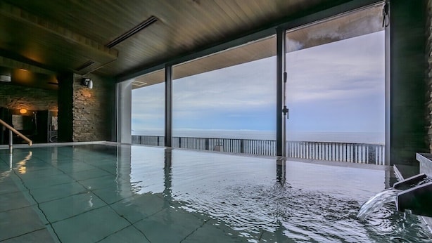 Una piscina interna con vista sul mare attraverso ampie finestre.