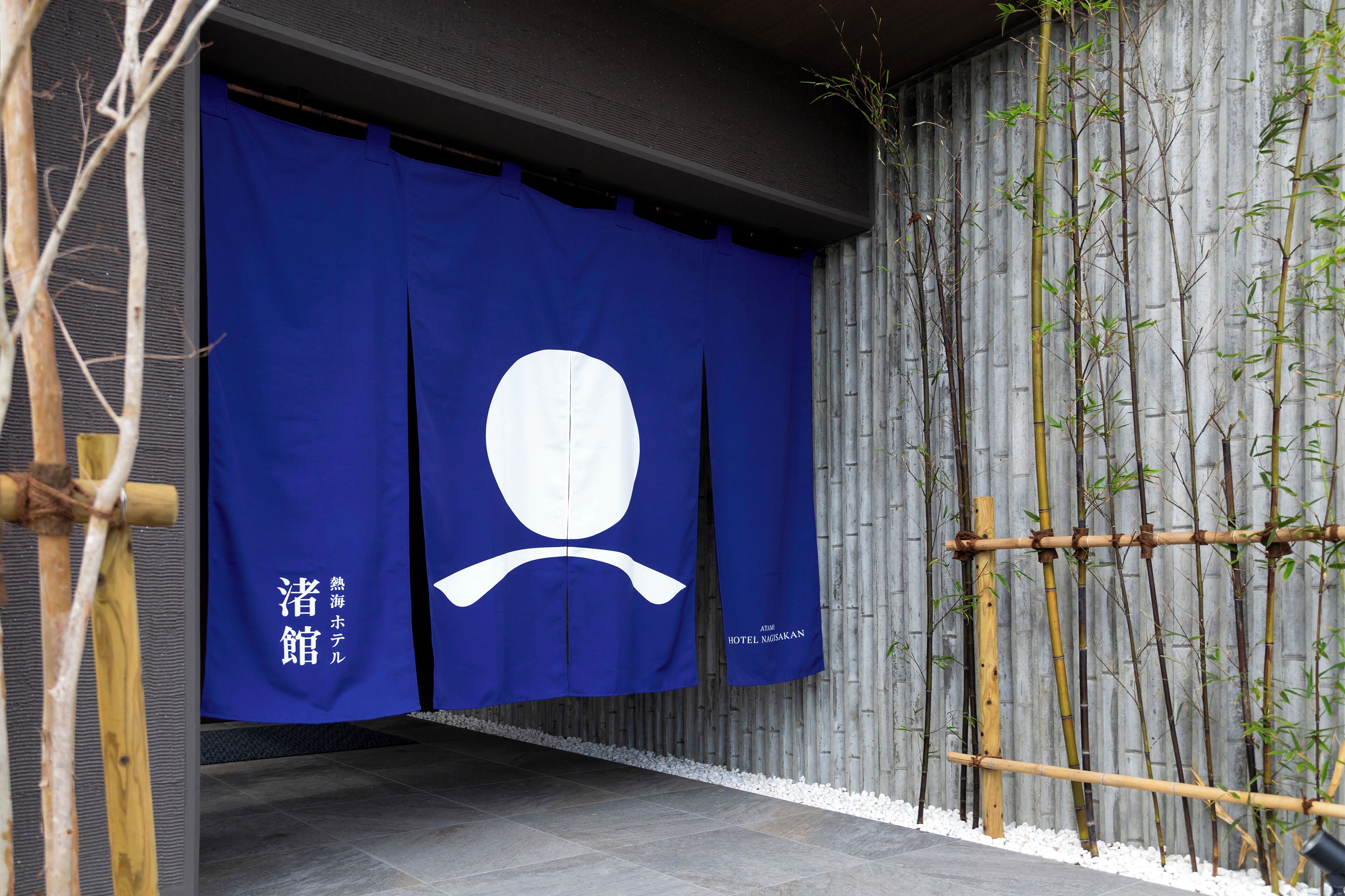 A blue entrance with a white emblem, bamboo plants, and a grey wall.