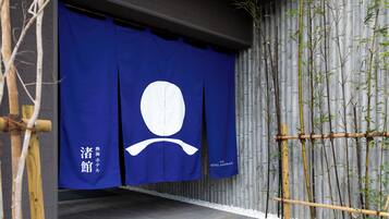 A blue entrance with a white emblem, bamboo plants, and a grey wall.