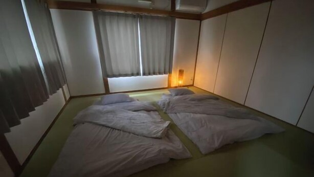 A traditional Japanese-style room with tatami flooring, a futon bed, sliding shoji doors, and a window with a view. - KaiTen house Jasmine (Beppu)
