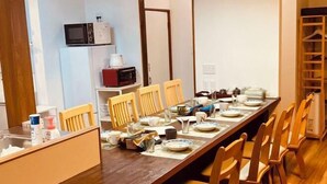 A long dining table with chairs, a microwave, and a coffee maker on the wall. - KaiTen house Jasmine (Beppu)