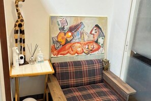 Une chambre avec un lit, un tableau accroché au-dessus de la tête de lit, une petite table avec des articles de toilette et une fenêtre.