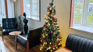 A living room with a Christmas tree, a black leather sofa, a round coffee table, and a window with a view of greenery. - KaiTen house Jasmine (Beppu)