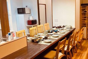 A long dining table with chairs, a microwave, and a refrigerator in the background. - KaiTen house Jasmine (Beppu)