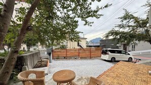 A patio area with wicker furniture, a wooden table, and a car parked nearby. - KaiTen house Jasmine (Beppu)