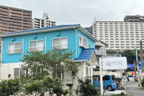 Um edifício azul com uma placa, um veículo azul e um prédio alto ao fundo.