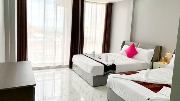 Habitación de hotel con dos camas, un escritorio y vistas a edificios a través del ventanal.