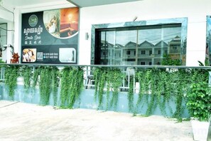 Fachada de edificio con un amplio ventanal, un cartel con texto e imágenes, y un balcón con plantas.