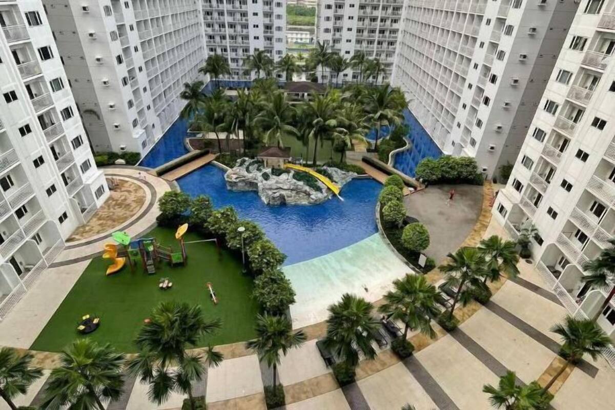 Un edifici residencial alt amb una piscina central, palmeres i una zona de jocs per a nens.