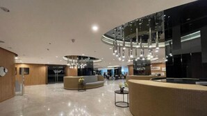 A modern lobby with a curved reception desk, seating areas, and a high ceiling with hanging lights. - MOA getaway staycations (Pasay)