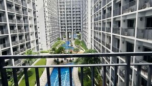 A high-rise building with multiple balconies, a central courtyard with a water feature, and a view of the surrounding area. - MOA getaway staycations (Pasay)