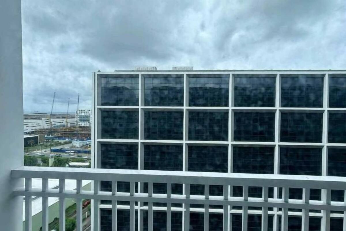 Edifici modern amb una estructura de finestres, un balcó amb barana blanca i un cel nuvolós.