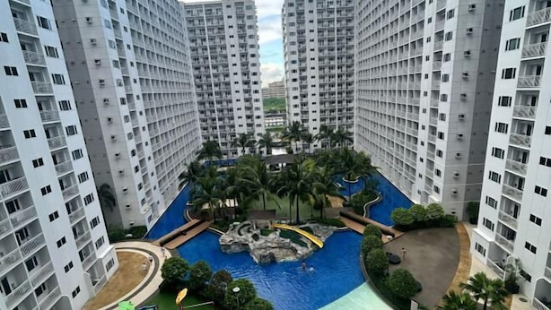 A high-rise residential building with a central swimming pool, surrounded by greenery and palm trees. - MOA getaway staycations (Pasay)