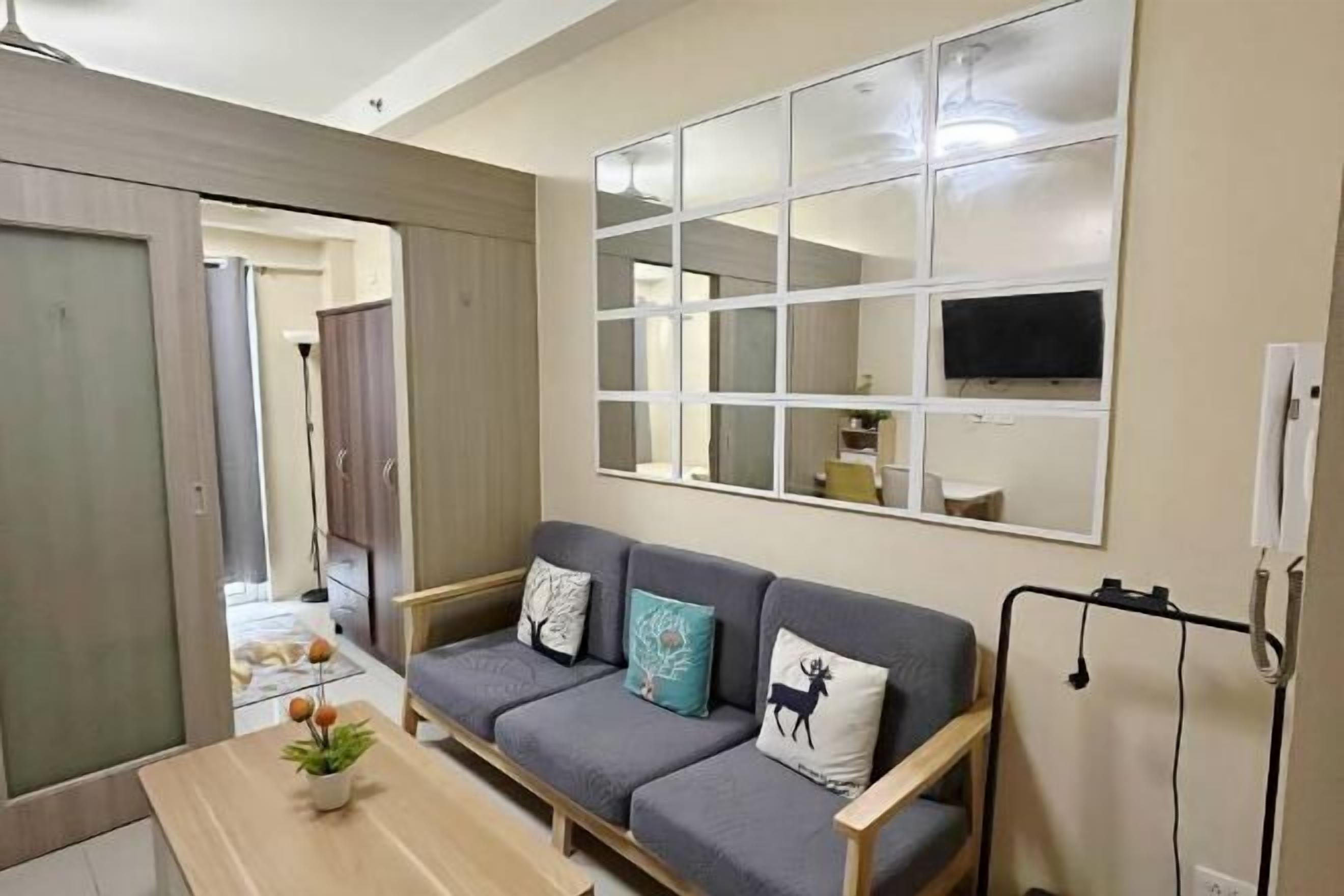 A modern living room with a grey sofa, a flat-screen TV mounted on a wall, and a wooden coffee table.