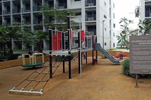 A children's playground with various play equipment, including slides and climbing structures, surrounded by a building with multiple floors and balconies. - MOA getaway staycations (Pasay)