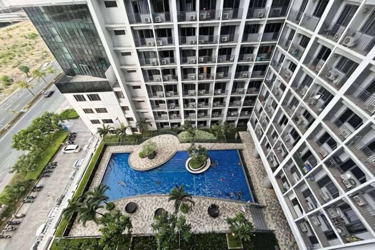 Un edifici alt amb piscina al terrat, múltiples balcons i una zona verda amb palmeres.