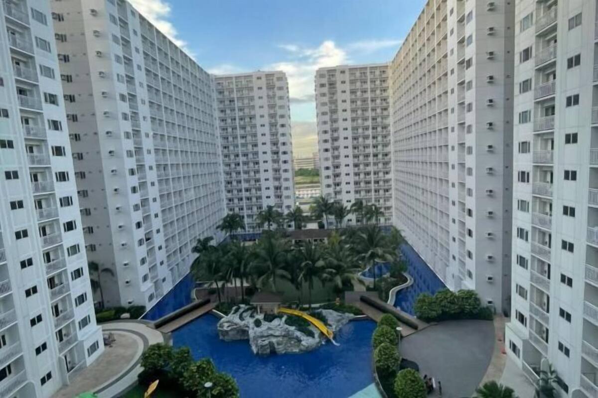 Un edifici residencial de grans alçades amb un pati central que compta amb una piscina, palmeres i una formació rocosa.