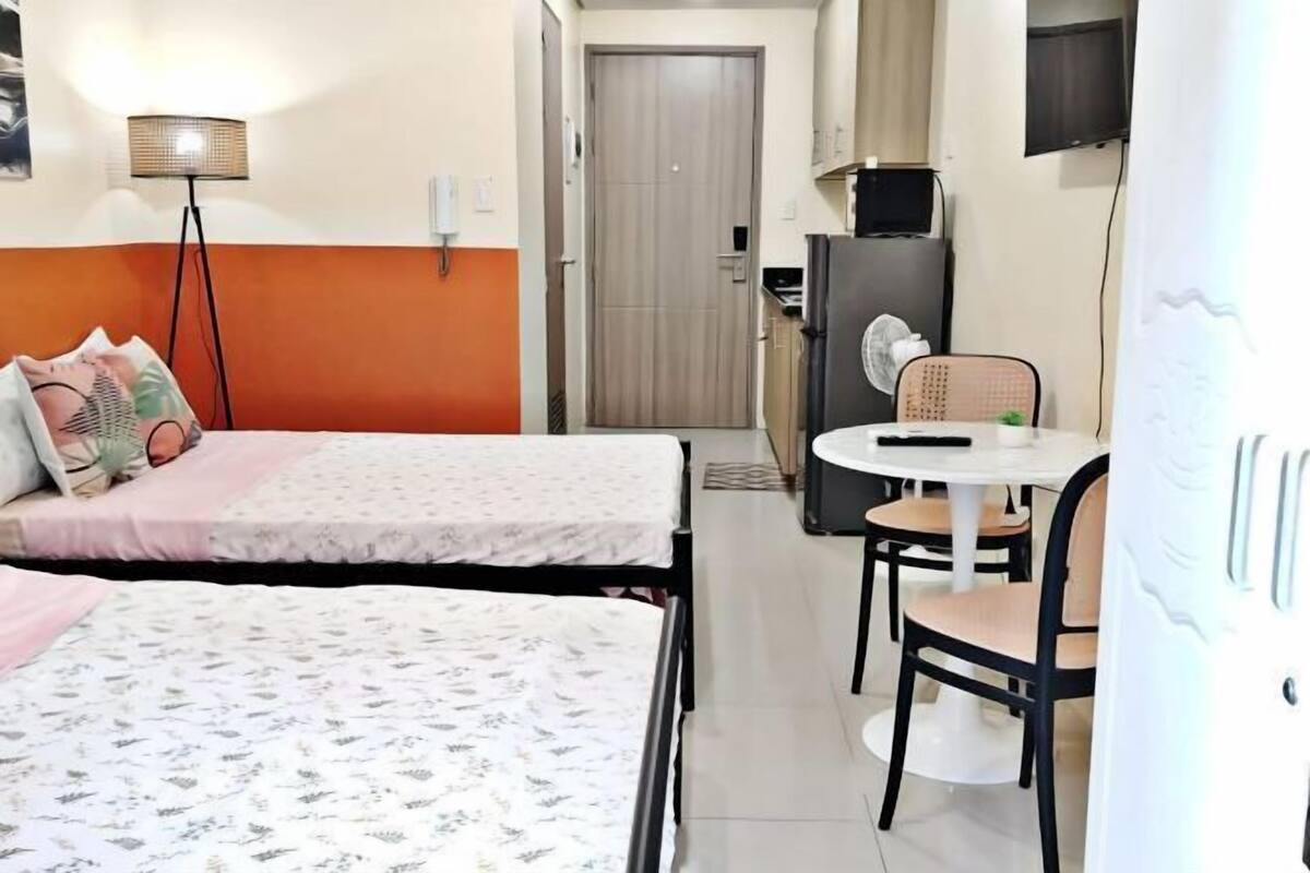 Habitació d'hotel amb dos llits, una taula de dinar amb cadires, un frigorífic i una televisió.
