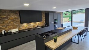 A modern kitchen with a stone backsplash, black cabinetry, and a wooden island. - Villa 200m²- swimming pool at the gateway to the Beaujolais region (Sainte-Euphémie)