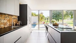 A modern kitchen with a stone backsplash, large windows, and a view of a swimming pool and garden. - Villa 200m²- swimming pool at the gateway to the Beaujolais region (Sainte-Euphémie)