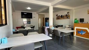 A modern dining area with tables and chairs, a reception desk, and a wall-mounted TV. - Lighthouse Inn Corporation former Lucky Tito D'mall Boracay (Boracay Island)