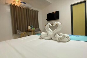 Una habitación de hotel con cama, televisor montado en la pared, escritorio con silla y cortina.
