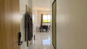 A hallway with a wooden door, a coat rack, a dining area with a table and chairs, and a large window allowing natural light. - Lighthouse Inn Corporation former Lucky Tito D'mall Boracay (Boracay Island)