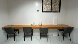 A conference room with a long wooden table, four chairs, a window with a patterned view, and a small table with items on it. - Lighthouse Inn Corporation former Lucky Tito D'mall Boracay (Boracay Island)