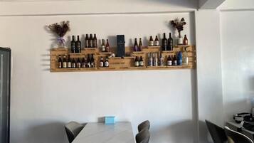 A dining area with a white table and chairs, a wine rack with bottles, and a small blue object on the table.