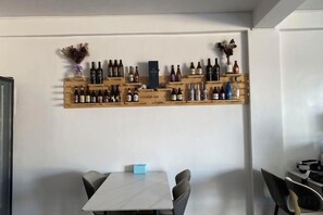 A dining area with a white table and chairs, a wine rack with bottles, and a small blue object on the table. - Lighthouse Inn Corporation former Lucky Tito D'mall Boracay (Boracay Island)