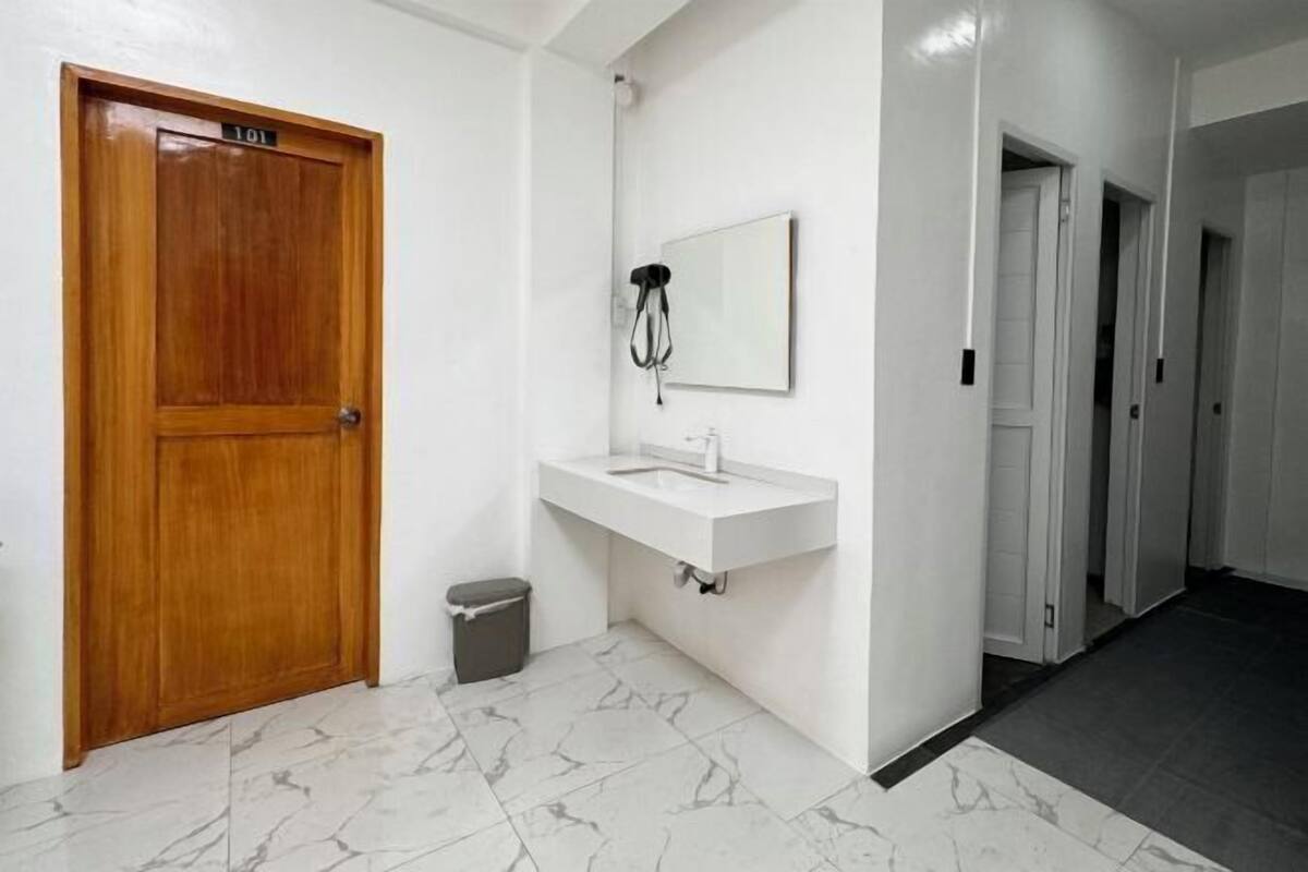 Ein Badezimmer mit Holztür, weißem Waschbecken, Spiegel und Mülleimer.