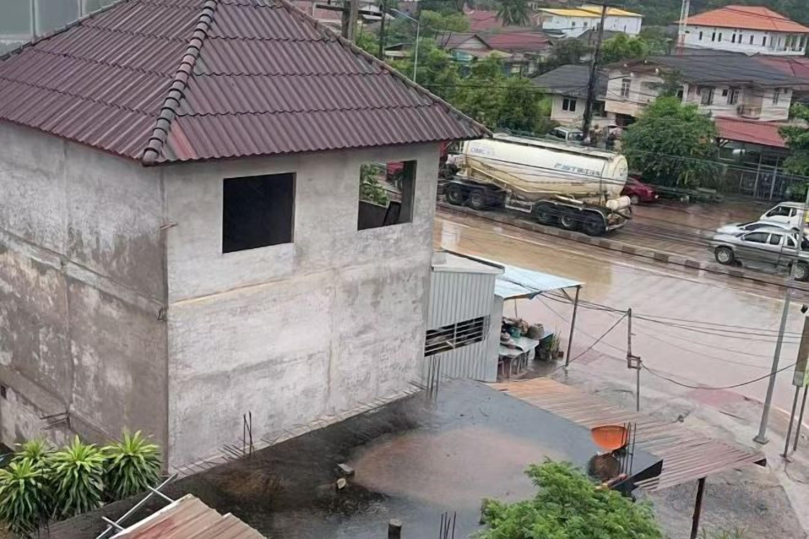 A concrete building with a metal roof, a small window, and a paved area with a metal structure.