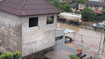A concrete building with a metal roof, a small window, and a paved area with a metal structure.