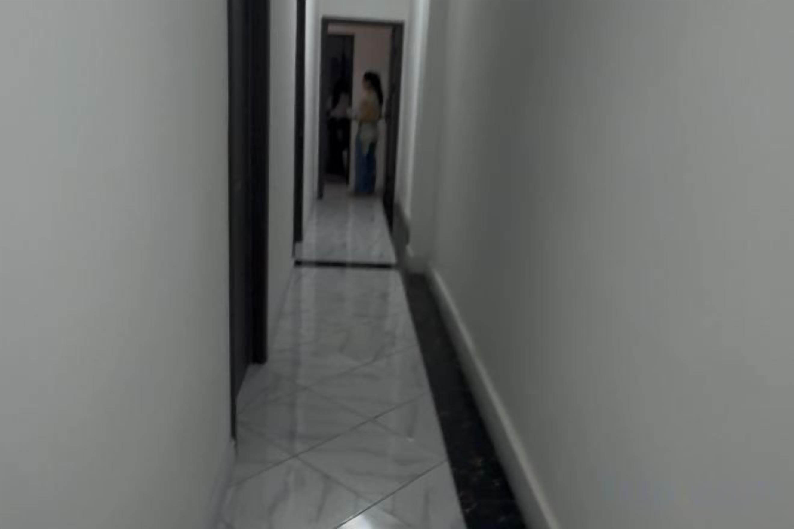 A narrow hallway with a tiled floor and a door at the end.