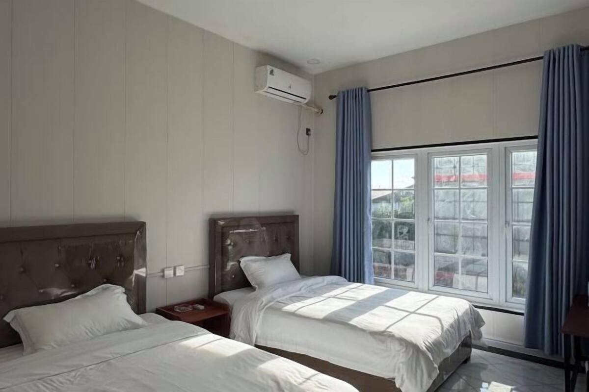 Une chambre d’hôtel avec deux lits, un appareil de climatisation, une fenêtre avec des rideaux et une vue sur l’extérieur.
