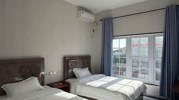 A hotel room with two beds, an air conditioning unit, a window with curtains, and a view of the outside.