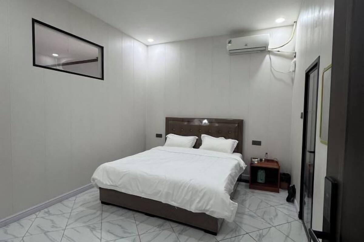 Une chambre à coucher comprenant un lit, une table de chevet, un appareil de climatisation et un tableau encadré accroché au mur.