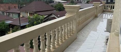 Un balcón con piso de baldosas y barandilla, con vista a una zona residencial con casas y construcción.