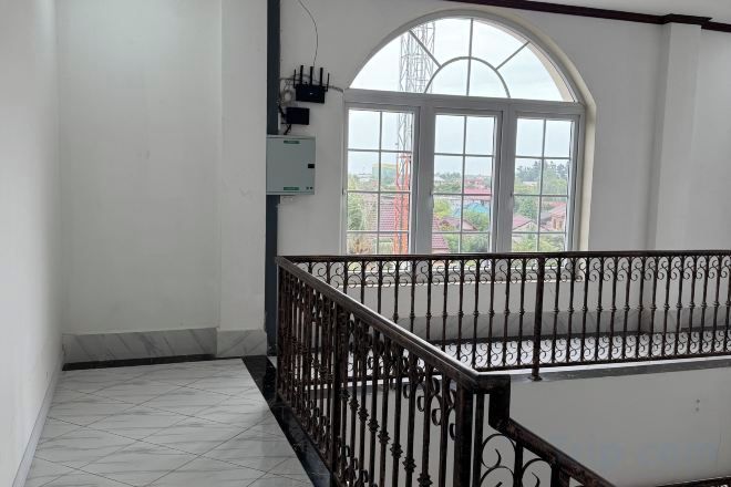 Una habitación con piso de baldosas, ventana con vista a edificios y baranda metálica.