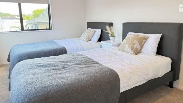 Quarto com duas camas, uma janela e mesa de cabeceira com planta.