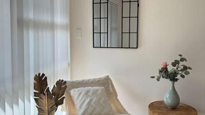 Um quarto com uma cadeira, um espelho e um vaso com flores.