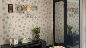 A hotel room with a polka dot wallpaper, a black console table with books and a tissue box, a potted plant, and a sliding glass door with a view of the outside. - MOZA HOUSE Wonosobo (Wonosobo)