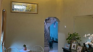 A hallway with a staircase, a framed artwork on the wall, a small table with a potted plant, and a mirror reflecting part of the room. - MOZA HOUSE Wonosobo (Wonosobo)