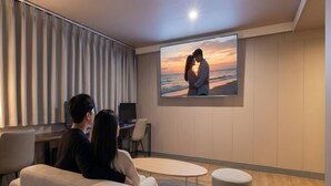 A couple sitting on a couch watching a sunset on a large screen. - Urban HOTEL&PLAY (Seoul)