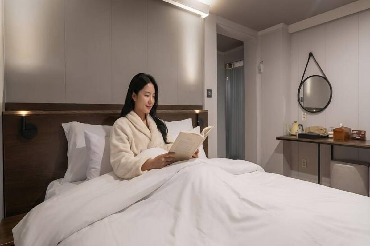 A hotel room with a bed, a bedside table with a lamp, a mirror, and a door.